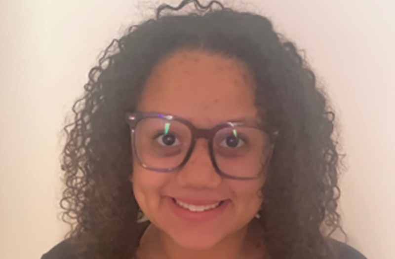 A headshot of a smiling woman with curly hair and glasses.